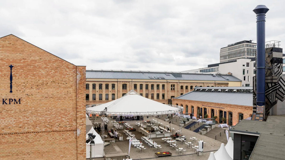 Städtischer Innenhof mit einem großen Zelt, umgeben von Gebäuden und bewölktem Himmel.