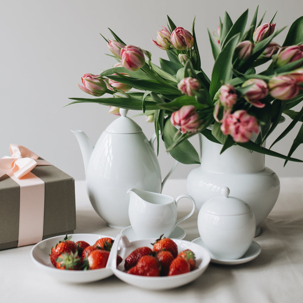 Blumenarrangement mit Teekanne, Sahnekännchen und Erdbeeren auf einem Tisch.
