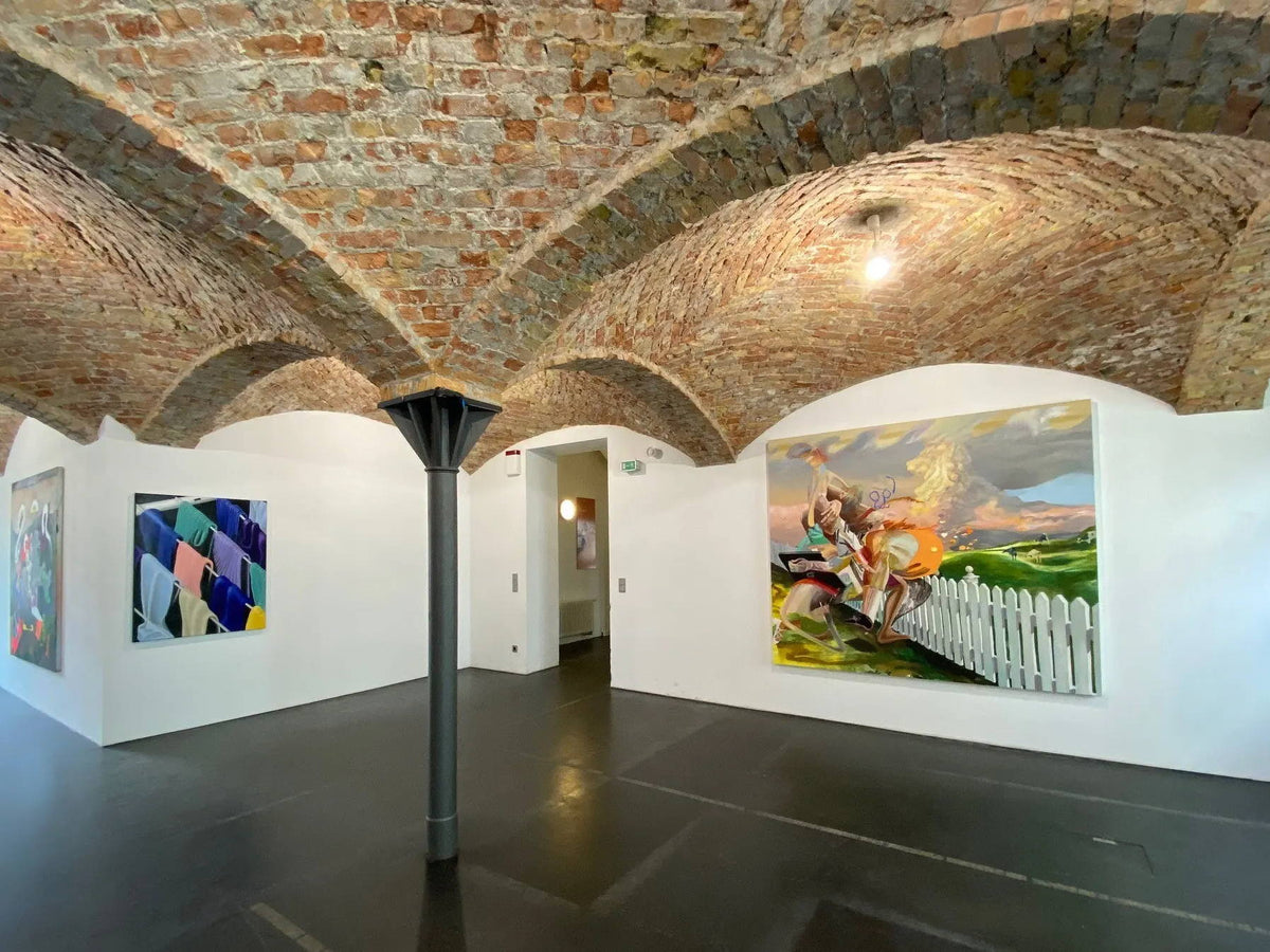 Kunstgalerie mit gewölbter Ziegeldecke und farbenfrohen Gemälden an weißen Wänden.