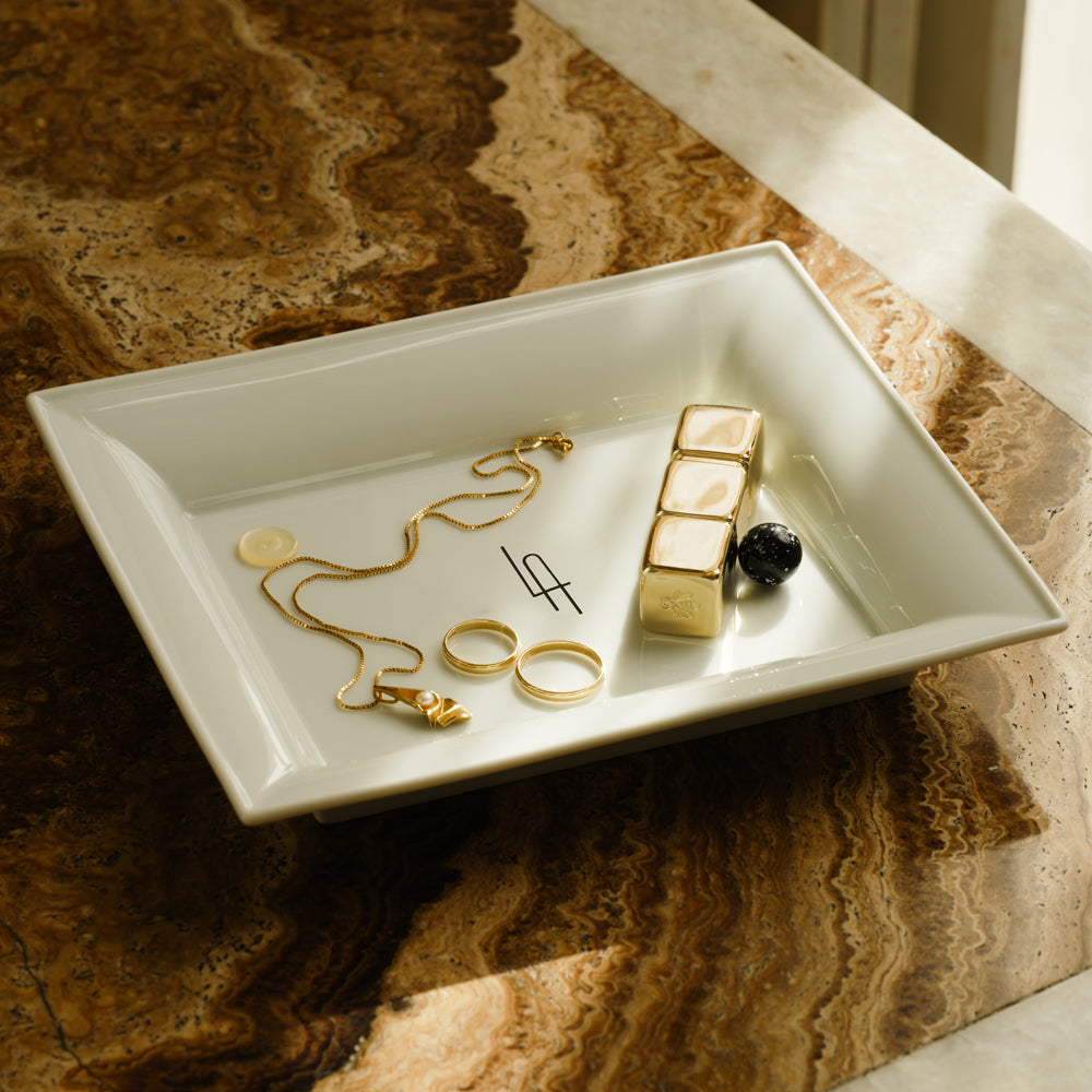 Eine weiße KPM Vide Poche mit Goldschmuck auf einer strukturierten Oberfläche.